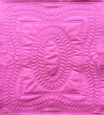 A bright pink whole cloth miniature quilt with a stencil design