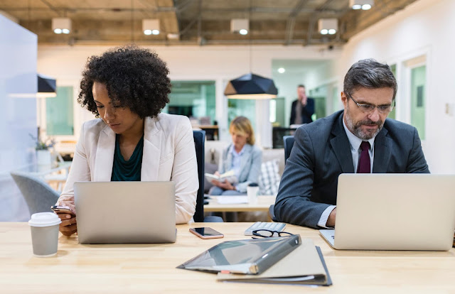 A man and a woman sitting in front of laptops