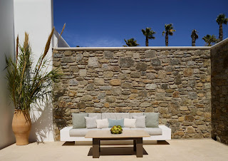 the terrace in bonzoe homes & villas with a sofa and a coffee table in front of a stoned wall