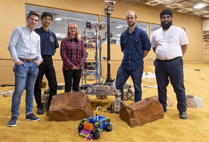 Picture of some of the elite team of graduate engineers with their rover (front), and the slightly bigger Airbus rover (back)