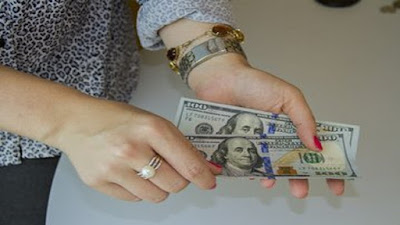 Two hands with wrist watch, bangle and ring holding out a couple of dollars bills.