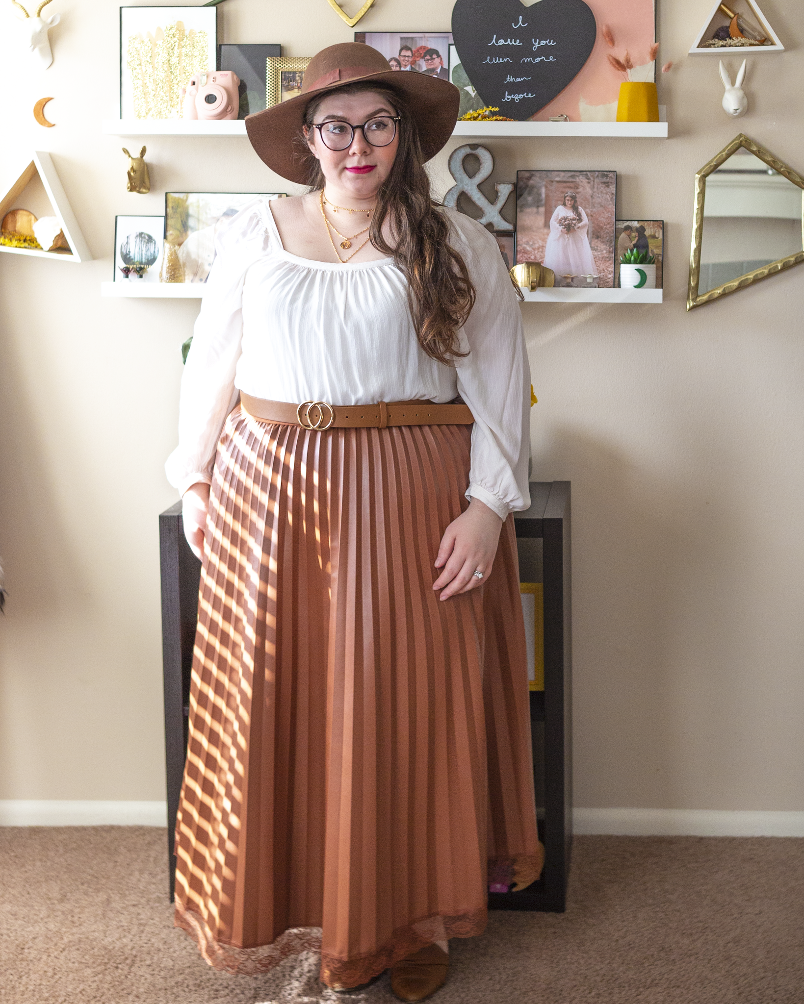 An outfit consisting of a dark brown wide brim floppy hat, a white square beck bishop sleeve blouse tucked into a cognac brown pleated maxi skirt and cognac brown d'orsay flats.