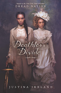 Two Black women in fancy cream and white clothing, the one on the left is holding a sword in her right hand, her sleeve and pant-legs are splattered with blood.