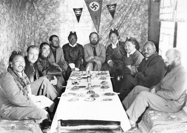 German and Tibetan men sitting around a table with food.