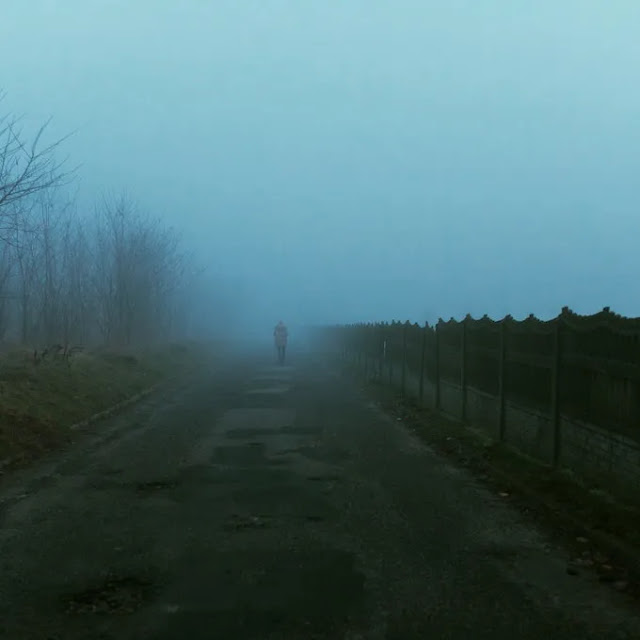A lonely girl walking in the foggy street alone.