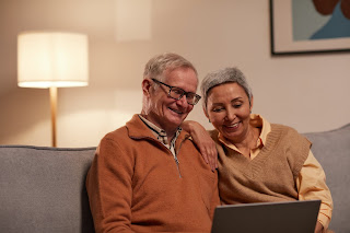 Two elderly people smiling while looking at a laptop.