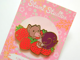 A photo of a pin badge, of a squirrel surrounded by strawberries and eating one of them