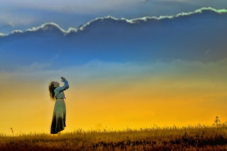 Girl with hands raised in worship against a sunset