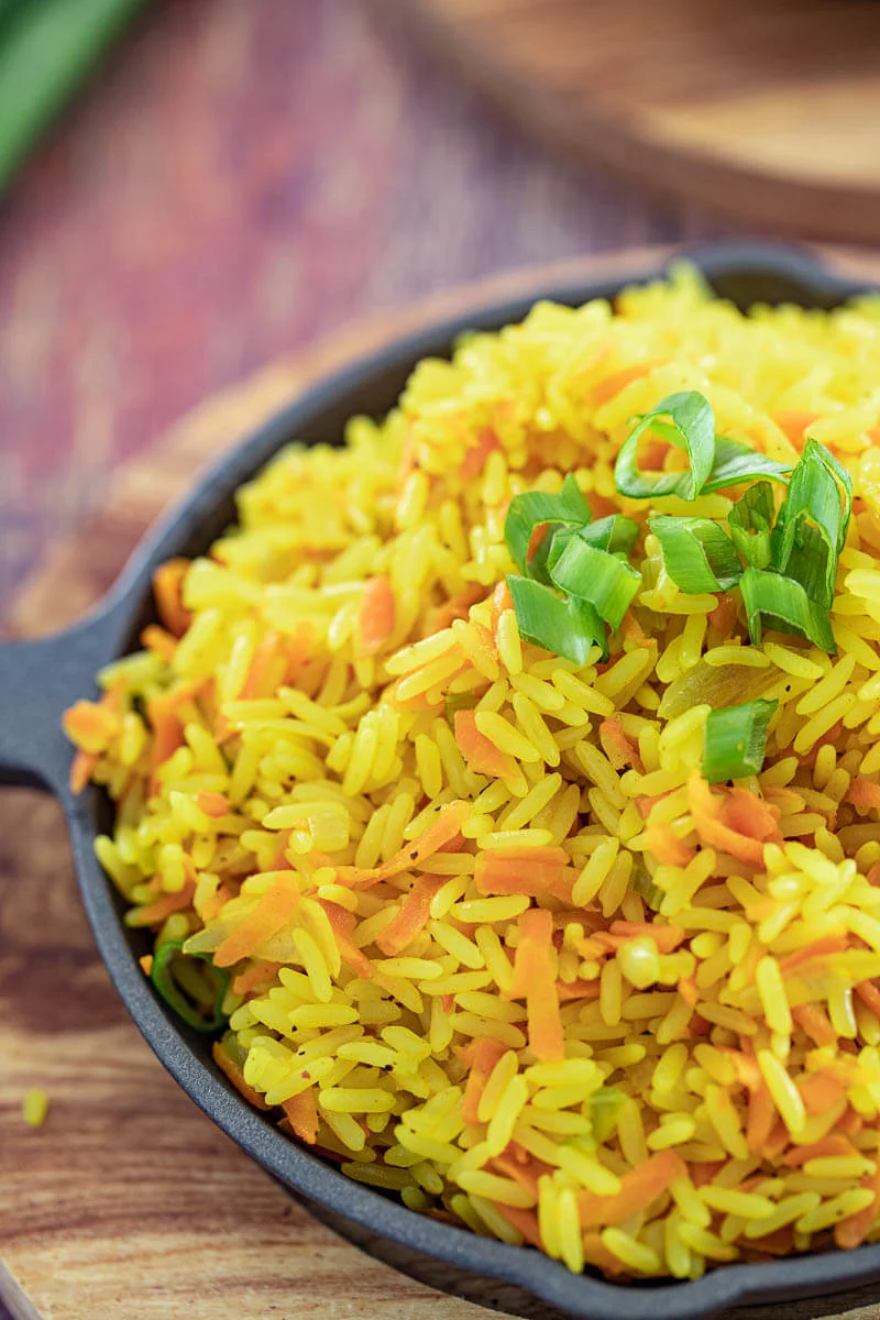 A clse up of carrot rice in a black serving dish, garnished with fresh chopped scallion.