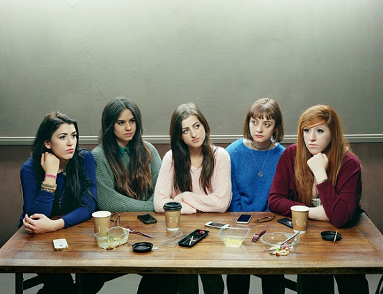 Retrato de 5 chicas sentadas a la mesa enajenadas unas de las otras, sus celulares frente a ellas, escena de distanciamiento social.