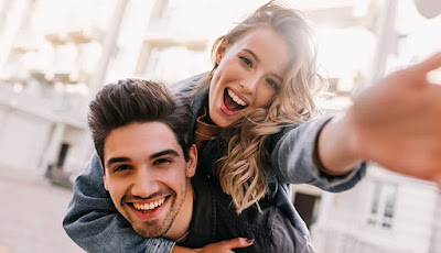 The girl is sitting on the boy's shoulder, both of them are very happy and are laughing.