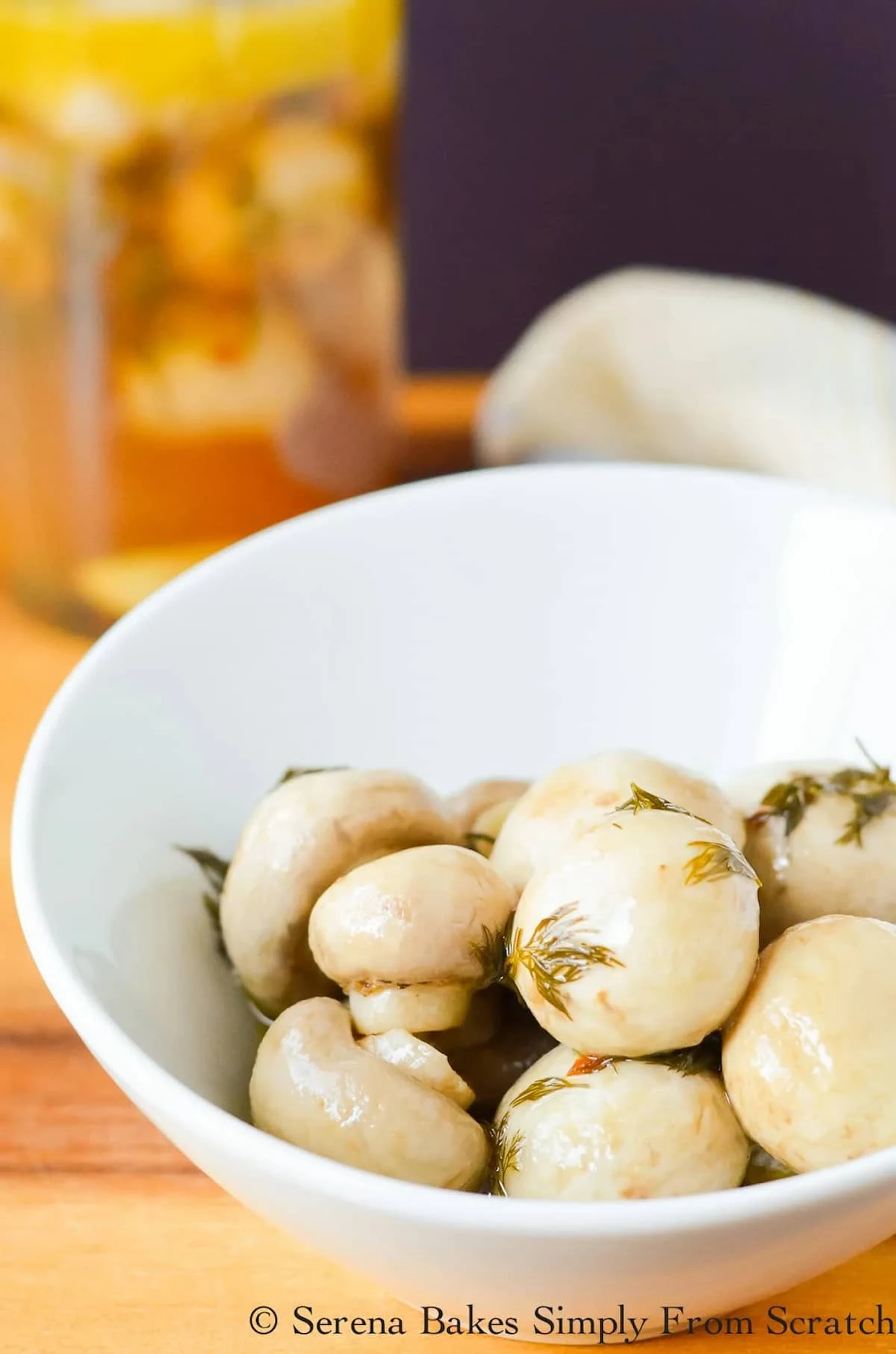 A white bowl full of Marinated Mushrooms with Marinated Mushrooms in a jar in the background.