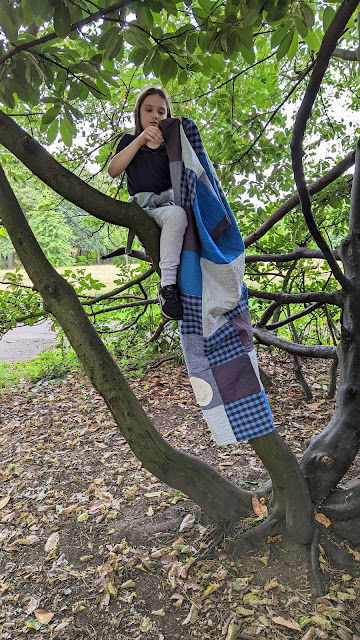 Girl holding quilt sitting on branch of a tree