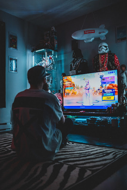 Man playing Fortnite in a darkened room with collectibles surrounding the TV