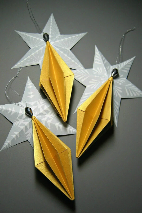 A trio of metallic gold paper Diamond Origami Ornaments resting on folded paper stars