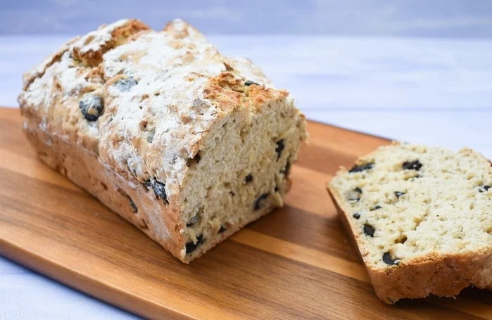 No Knead Black Olive Beer Bread on wooden board with slice of bread cut, showing inside of bread