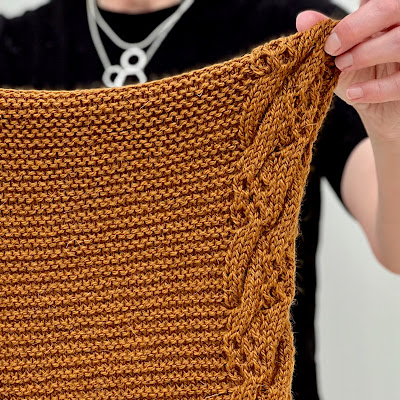 Emma is holding a section of shawl towards the camera showing the cable pattern