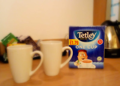 Two white mugs faded out in the foreground a bag of Tetley tea bags behind in focus.