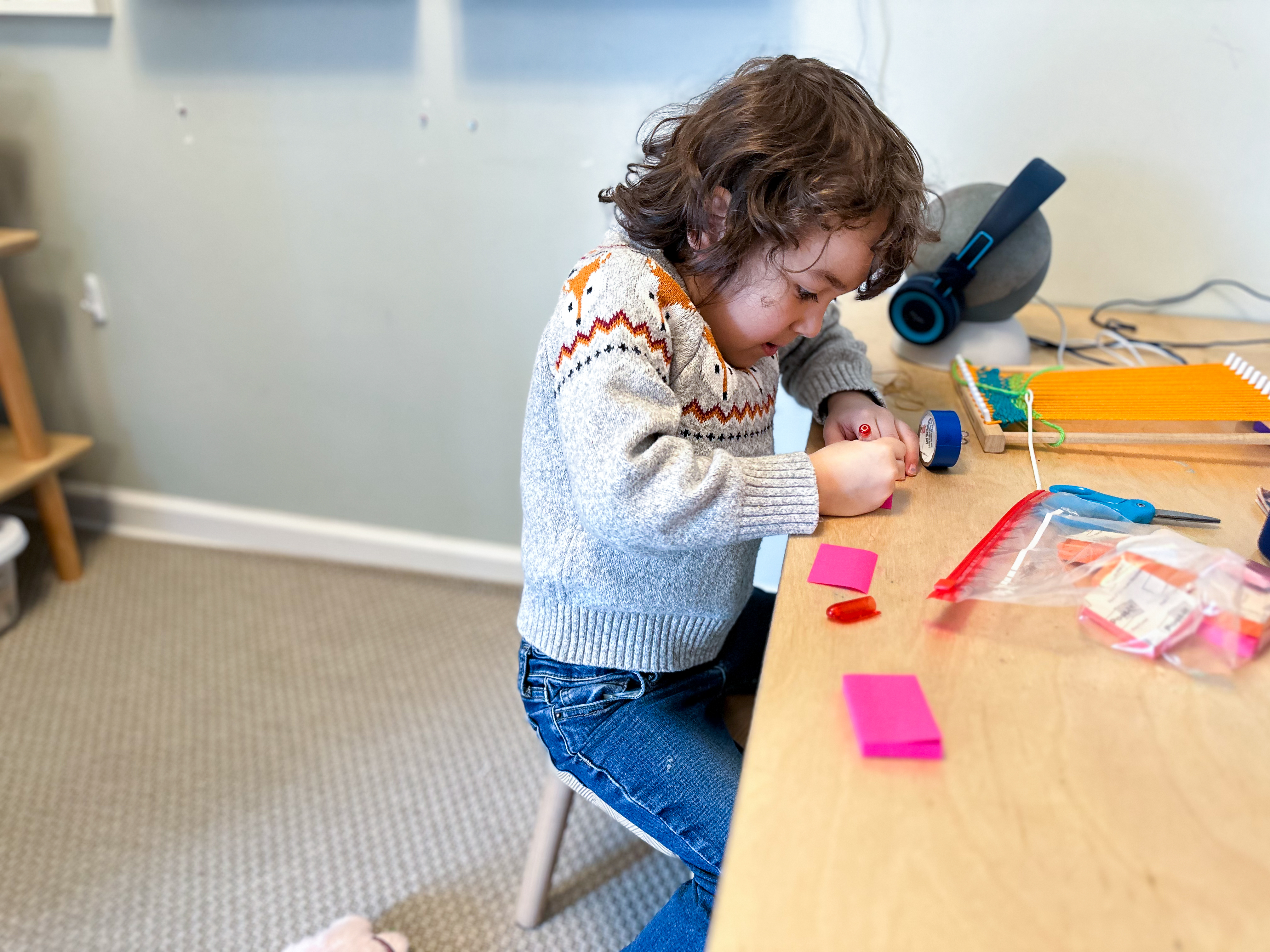 Kindergarten child sits at table in Montessori home and uses post-it notes to practice writing