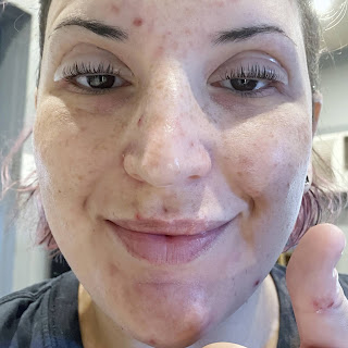 Close up of Lara's face after applying lift pads and gluing lashes to them on both eyes. She is looking directly at the camera, smiling and giving a thumbs up.