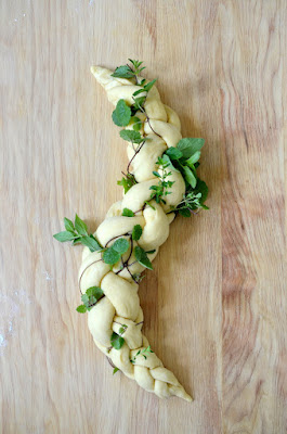 Ein Vierstrang-Zopf aus Hefeteig ist mit frischen Kräutern dekoriert und wartet auf den Backofen.