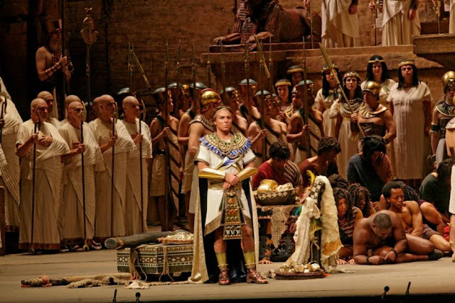 foto de cena da Ópera Aida de Verdi, mostra-se o Faraó em primeiro plano e seus servidores atrás