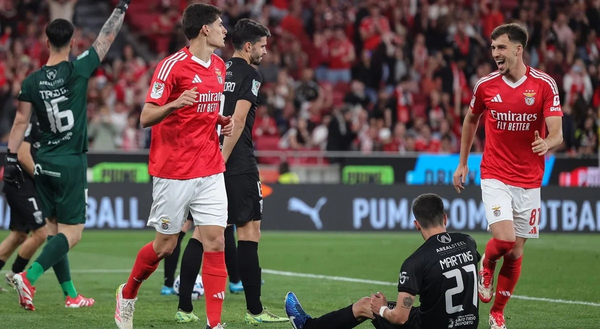 Jogadores do Benfica comemorando após um gol em um jogo emocionante, Benfica x Tirsense com a torcida vibrando ao fundo e adversários ao chão.