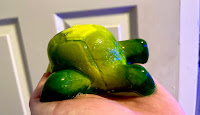 A white hand holding a large splayed out large green turtle shaped shower jelly on a bright background