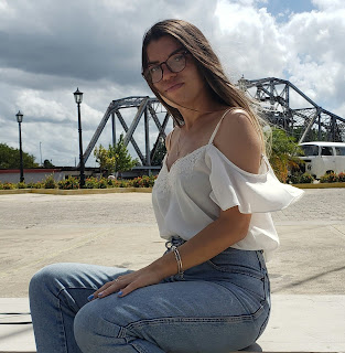 Cubana sentada puesta pantalon jean, blusa negra, mirando de perfil