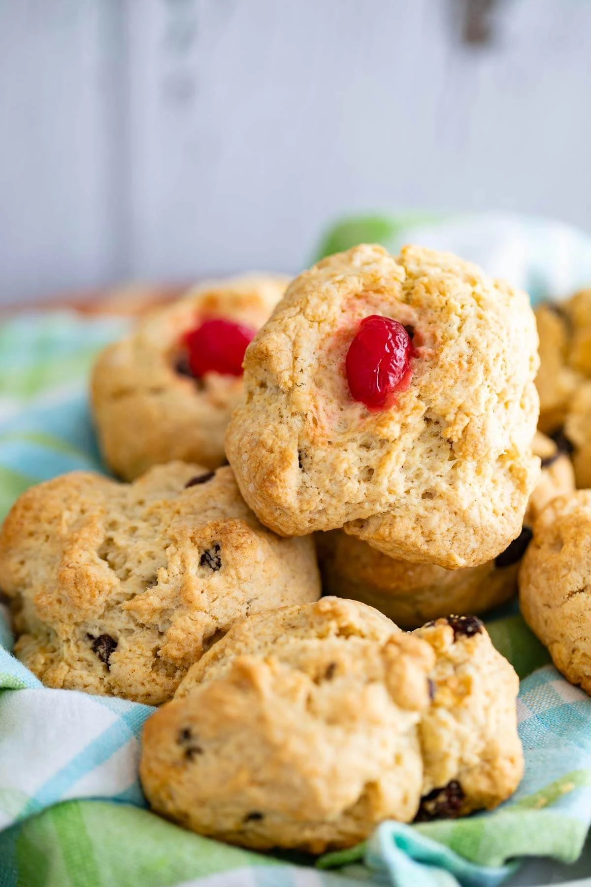 A tray of rock buns on a plaid serving sheet with one bun having a cherry in the middle.