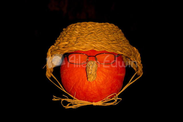 An orange pumpkin wearing glasses and hat on black background