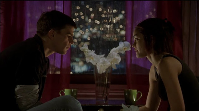 Film still from 40 days and 40 nights. A man and a woman look at one another. White flowers sit between them.