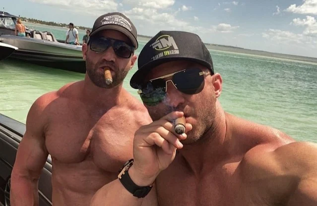 Two sexy Italian dudes wearing sunglasses from the chest up smoking cigars on a boat