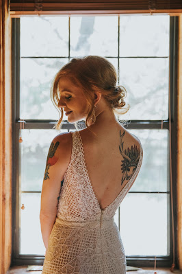 Novia posando en una ventana, con el cabello recogido para mostrar el escote en la espalda y los tatuajes