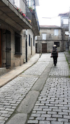 peregrina de Santiago andando numa ruela com casas de pedra ao redor