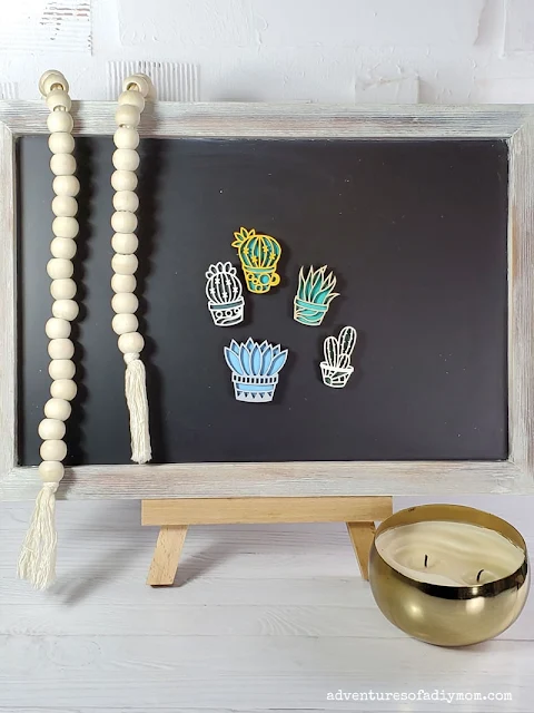 Laser cut succulent magnets staged on a chalkboard for decoration with wood beads and a brass bowl candle.