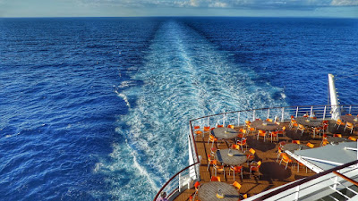 The stern of a cruise ship with tables and chairs laid out. The wake of the ship on the water visible.