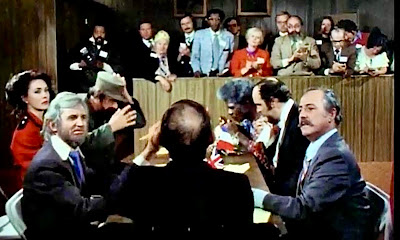 Scene from The Dicktator  shows The president of the United States sits at the head of a table full of rulers from around the world as the reporters  look on.