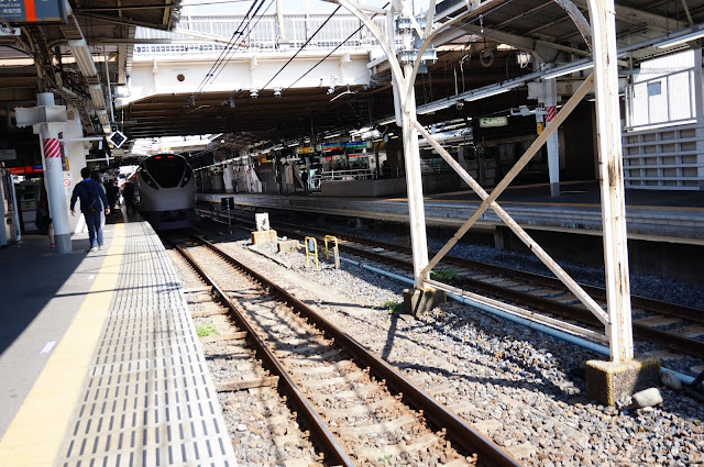 Guy walking towards a bullet train (shinkansen) in Tokyo with a view of the rails and the platform