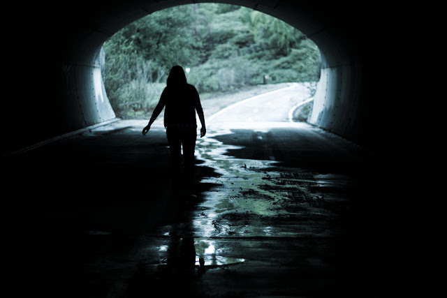 Chica caminando a contraluz en la oscuridad de un túnel