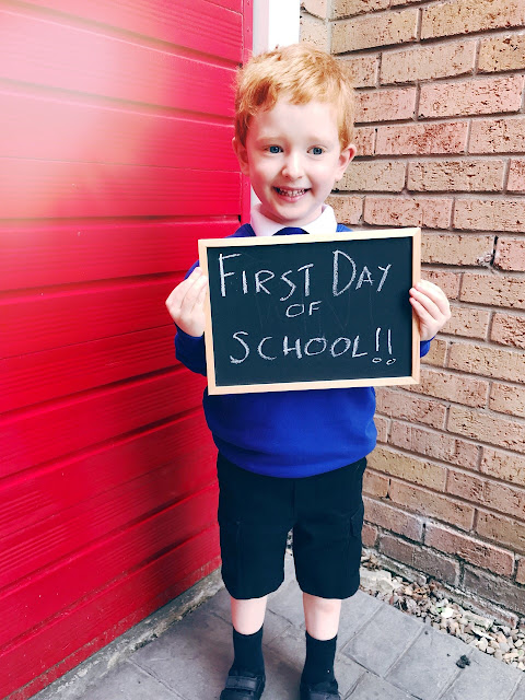 Little boy dressed in a school uniform holding up a sign that says first day of school