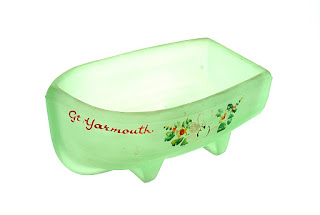 A green glass boat trinket with floral decoration and Great Yarmouth painted on it