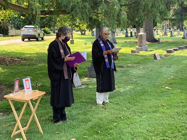 Two female Buddhist priests chant sutras at portable altar in graveyard