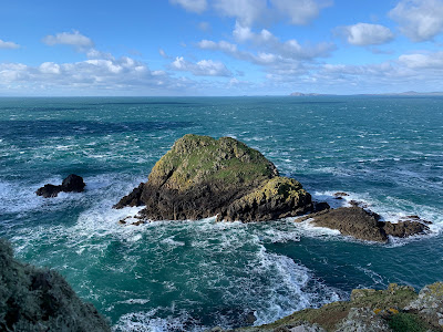 A large rock in a windswept sea against bright blue skies