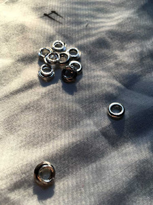 A small pile of silver grommets on palest aqua fabric with an eff in black marker.