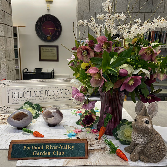 An Easter display featuring a vase full of hellebores and white forsythia.