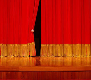 Arm reaching out to slightly open the red curtain on stage