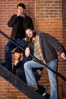 photo of three men posing in front of a brick wall