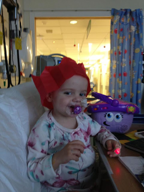 A little girl wearing a Christmas cracker hat, whilst in a hospital bed