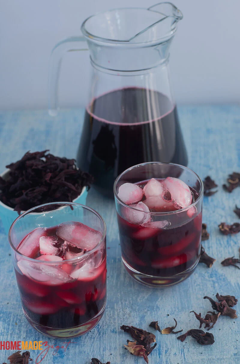 A jug of Caribbean sorrel drink with two glasses of sorrel with ice.